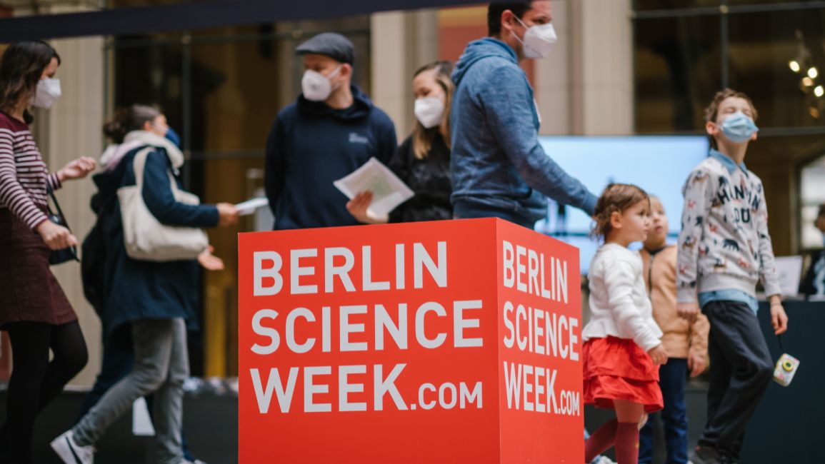 Eine Gruppe von Menschen laufen hinter einem großen roten Schild der Berlin Science Week vorbei.