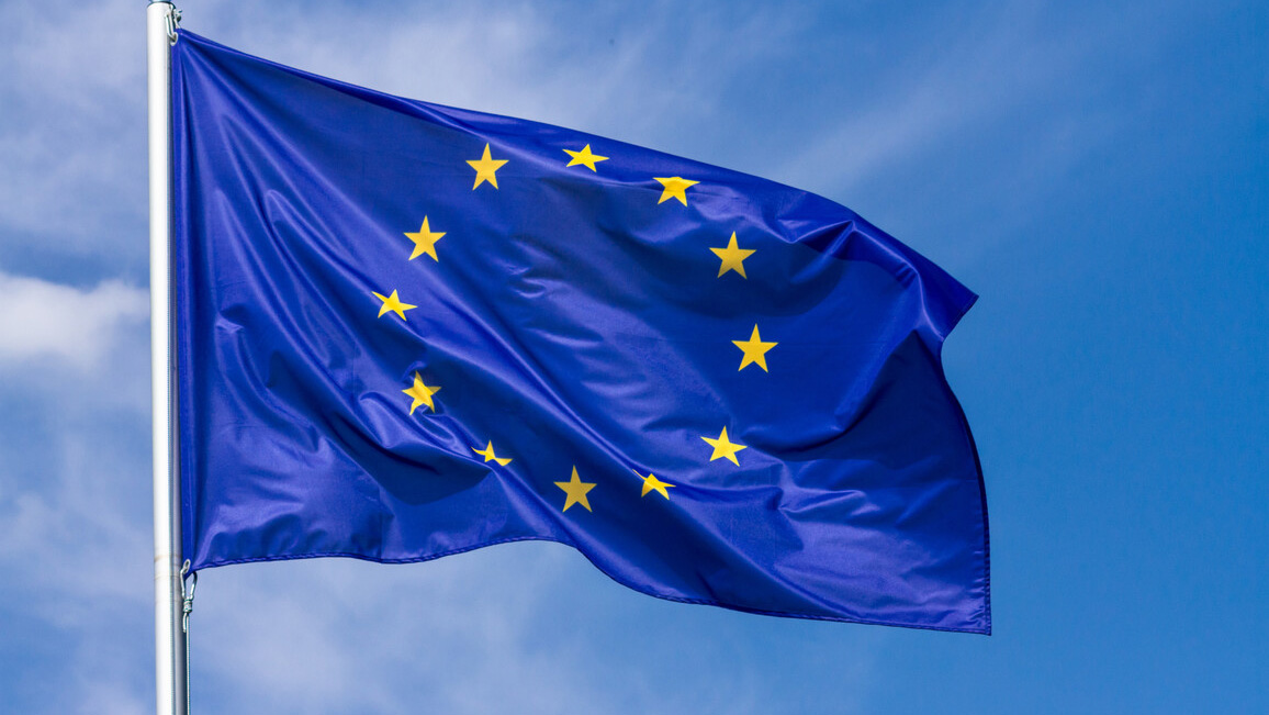 Eine EU-Flagge flattert an einem Fahnenmast. Im Hintergrund ist der blaue, leicht bewölkte Himmel zu sehen.