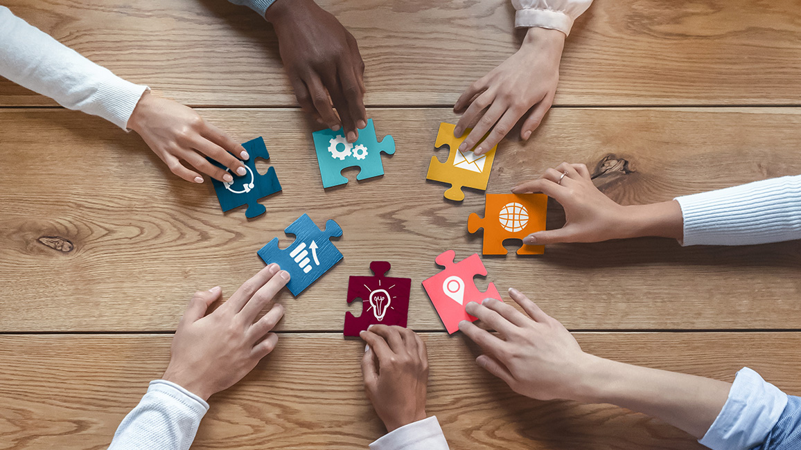 H&auml;nde verschiedener Personen setzen bunte Puzzleteile zusammen.