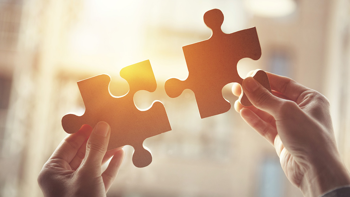 Zwei H&auml;nde halten zwei Puzzle-Teile nebeneinander, um sie zusammenzusetzen.