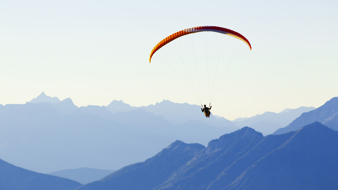 In the distance, there is a paraglider in front of a mountain panorama.