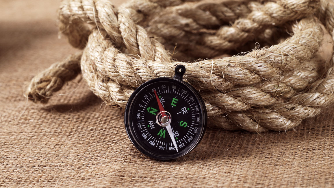 Ein Kompass lehnt an einem zusammen gerollten Seil.