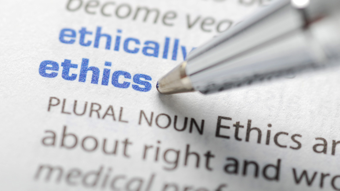 Closeup view on an entry in a dictionary. A pen points on the word "ethics".