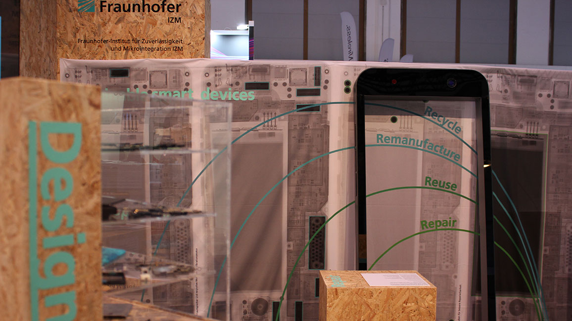 Stand des Fraunhofer-Institut für Zuverlässigkeit und Mikrointegration auf der IFA 2022. Aufgebaut sind Modelle von Smartphones sowie in Schaukästen deren Innenleben. Vor dem großen Modell einer Smartphonehülle ist eine Glaswand mit den Schriftzügen Recycle, Remanufacture, Reuse und Repair, jeweils oberhalb geschwungener Linien zu sehen.