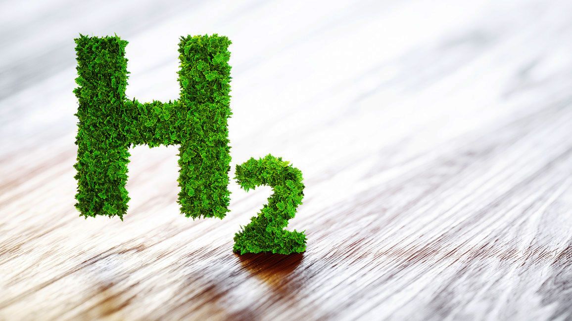 Das Symbol H2 ist mit grünen Blättern bedeckt. Im Hintergrund ist eine helle Holzfläche zu sehen.